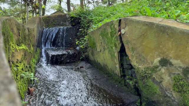 A small waterfall flows in an irrigation canal with cracks on the sides. Perfect for Nature videos or flowing water ASMR loops.