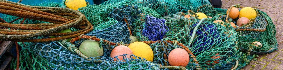 Large pile of industrial grade fishing nets, rusty metal cables, and yellow and orange floats,...