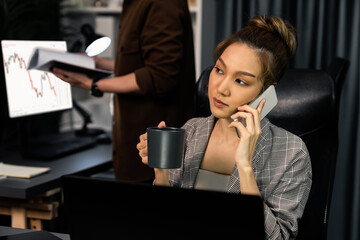 Businesswoman calling with customers to make new project job at modern office while coworker checking paperwork folder of business plan to database report meeting at over late night time. Infobahn.