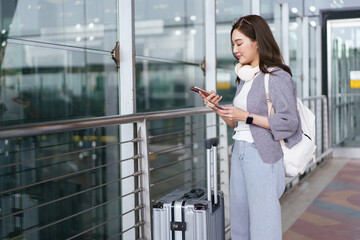 Smiling traveler walking out of an airport with luggage and a smartphone.