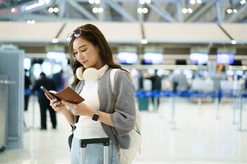 Asian woman holding passport and smartphone inside an international airport.