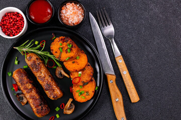 Grilled meat and vegetables served on a black plate with sauces and spices in a modern kitchen setting at lunchtime