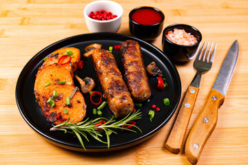 Grilled sausages served with roasted vegetables and sauces on a black plate at a dining table