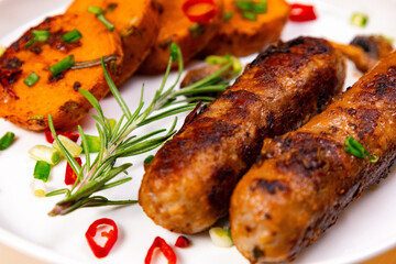 Grilled sausages and roasted vegetables on a white plate are prepared for a meal at a gathering during a summer afternoon