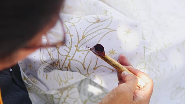 Artisan drawing traditional Indonesian batik pattern on fabric