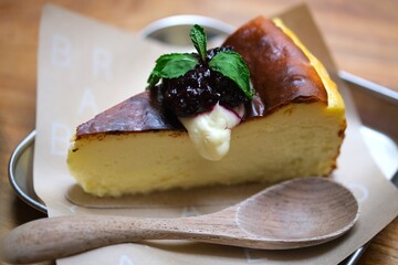 Creamy cheesecake slice topped with berry compote and mint leaves, served on parchment paper with a wooden spoon for a cozy dessert presentation. © Ahmad