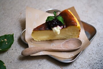 Creamy cheesecake slice topped with berry compote and mint leaves, served on parchment paper with a wooden spoon for a cozy dessert presentation. © Ahmad
