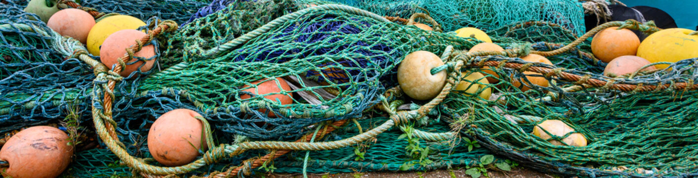 Large pile of industrial grade fishing nets, rusty metal cables, and yellow and orange floats, commercial fishing industry, storage at port in Scotland, UK

