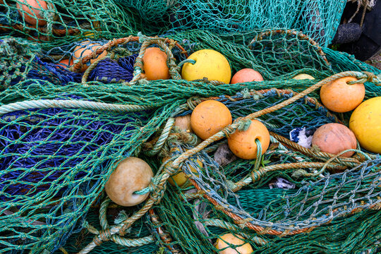 Large pile of industrial grade fishing nets, rusty metal cables, and yellow and orange floats, commercial fishing industry, storage at port in Scotland, UK
