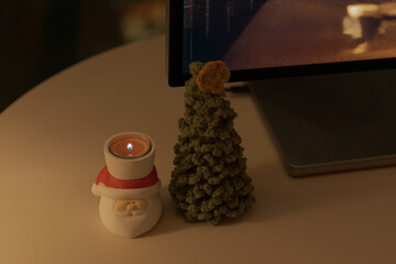Santa candle holder and a small pine tree figurine grace a cozy table near a computer