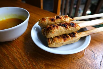 Traditional Balinese sate lilit made from minced seasoned meat wrapped around lemongrass sticks, served on a plate with flavorful dipping sauce.