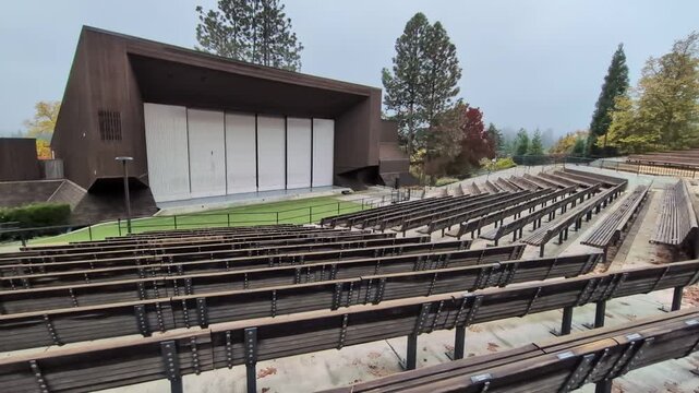 Video of an empty outdoor theatre showing huge stage, a tall metal backdrop, and endless rows of seats framed by colorful fall trees, capturing the scale and beauty of this beloved venue.