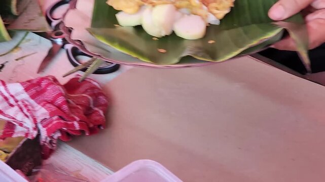 Traditional pecel street food wrapped in banana leaf by hand. Indonesian pecel preparation with banana leaf street food style. Authentic pecel serving process with hands and banana leaf