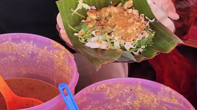 Fresh pecel street food served with peanut sauce in banana leaf. Traditional Indonesian pecel with peanut sauce in vibrant colors. Hand-served pecel with peanut sauce on banana leaf street food