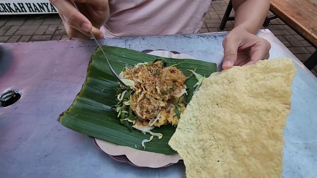 Enjoying traditional Indonesian pecel with rice crackers on top. Authentic Indonesian pecel served with crispy crackers and sauce. Tasting fresh pecel street food with crunchy crackers on banana leaf