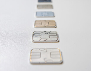A close-up of several SIM card chips arranged in a row on a white textured surface. The foreground chip is in sharp focus, with others blurring into the distance.
