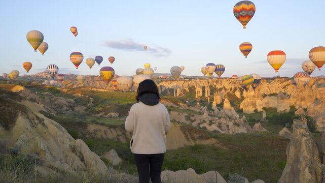Woman enjoying hot air balloons flying over Cappadocia at sunrise in Turkey