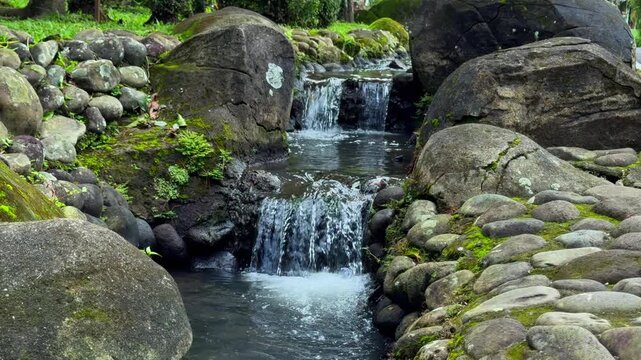 Cascading water flows gently over moss-covered rocks in a tranquil natural stream. Nature Video or flowing water ASMR loops.