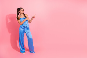 Young chic female model in blue jumpsuit poses pink backdrop smiling pointing to illustrate fashion lifestyle and shopping themes modern stylish branding marketing