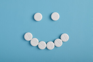 White pills arranged in a smiley face shape on a blue background, symbolizing the positive effects of the treatment.