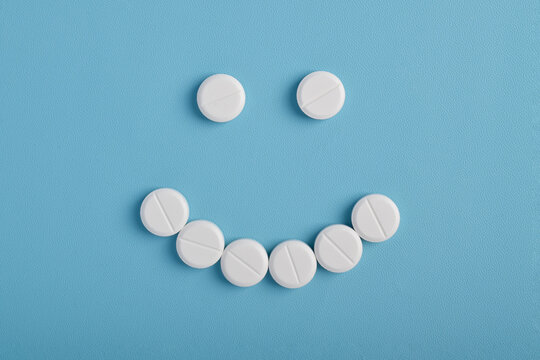 White pills arranged in a smiley face shape on a blue background, symbolizing the positive effects of the treatment. - Powered by Adobe