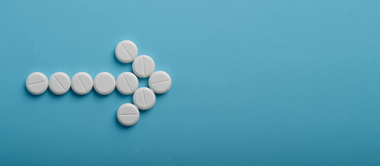 Medical pills in arrow shape pointed towards the right on blue background, with copy space for your design.