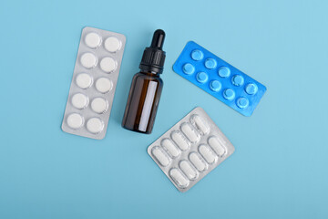 Tablets, pills and glass serum dropper bottles isolated on blue background. top view