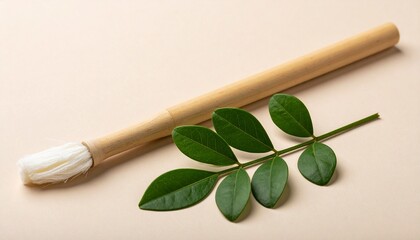 Calligraphy brush with white bristles beside green branch on beige background, symbolizing harmony of art and nature.