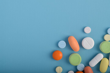 Various colorful pills and capsules form a frame, isolated on a blue background, copy space for...