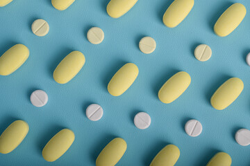 Pattern of white and yellow medical pills arranged neatly on a blue background, creating a modern pharmaceutical layout suitable for healthcare and medication concepts.