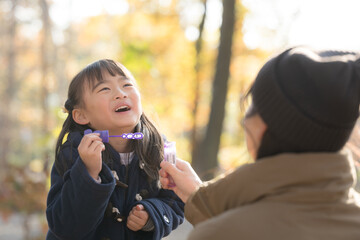 シャボン玉を秋の公園で遊ぶ親子　若いお母さんとかわいい娘　子育てや育児の幸せイメージ