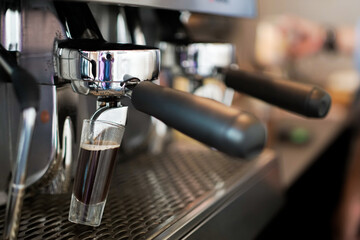 Close-up shot of espresso flowing from a portafilter into a glass on a professional coffee machine, showcasing barista workflow, café atmosphere, and specialty coffee preparation