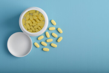 Bottle and vitamin pills isolated on blue background, top view. Concept of pharmacy, medicine, vitamins, food supplements.