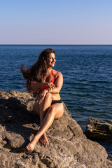 Woman rocks ocean, smiling woman sitting on sun-drenched coastal rocks enjoying summer vacation with copy space