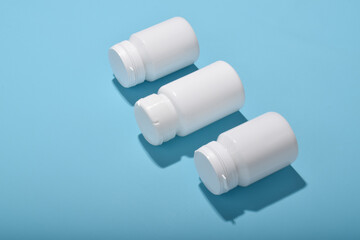 Three white medicine bottles on blue background, concept of pharmacy, healthcare products and medical supplies.