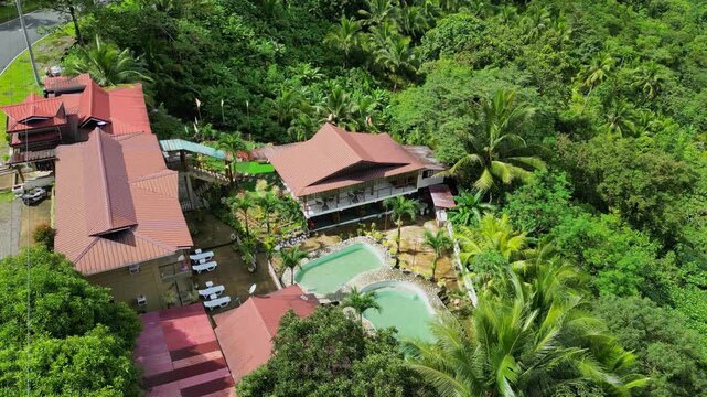 Passing top view aerial of resort compound with red roofs and pool surrounded by tropical forest beside Marcos Highway in Tanay Rizal, Philippines.