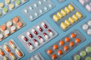 Various medicine capsules, pills and tablets in blister packs isolated on blue background, top view. Health and medicine concept.