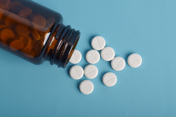 White medical pills and tablets spilling from a medicine bottle on a white background, top view,...