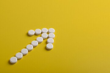 Medical pills in arrow shape pointing to the top right on yellow background, with copy space for...