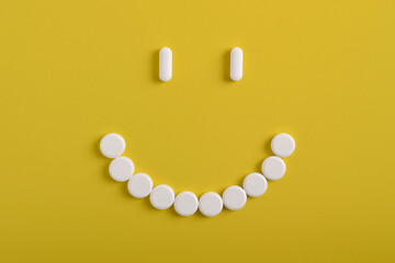 White pills arranged in a smiley face shape on a yellow background, symbolizing the positive effects of the treatment.
