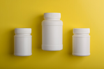 Three white medicine bottles on yellow background, concept of pharmacy, healthcare products and medical supplies.