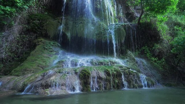 Low drone glides toward mossy Kurdish waterfall with fast flowing streams.