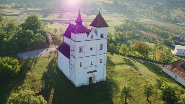 Drone of the historic white church in Herina, Bistrita Nasaud, Romania, with red roofs, in a quiet and foggy morning valley.