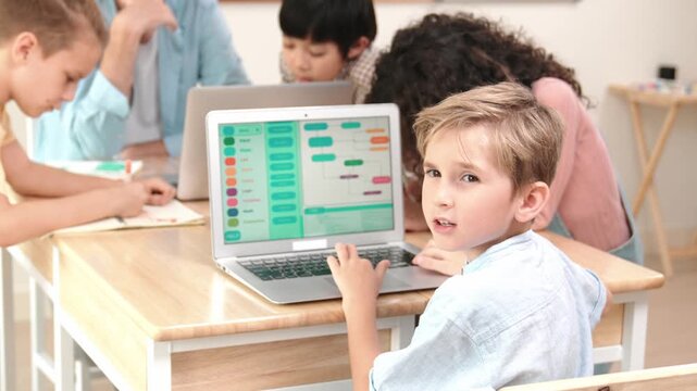 Smart caucasian boy turn around and looking at camera in STEM technology class while group of diverse student and teacher doing mind mapping. Smart child learning coding software program. Pedagogy.