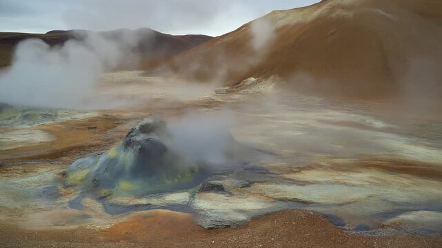 Geothermal landscape with steaming mud pots and fumaroles in a barren, colorful volcanic area.