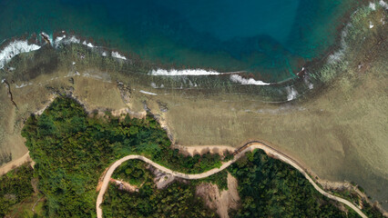 Vertical top-down drone shot showing textured coral reef shallow turquoise water and coastal road winding through green vegetation in Barangay Cheey Busuanga Island Philippines