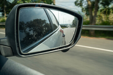 Fototapeta premium Close-up of a side mirror reflecting a highway on a sunny day.