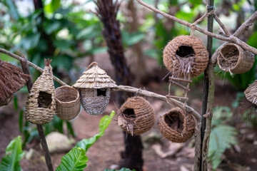 Handmade birdhouses crafted from natural materials hanging on a tree branch.