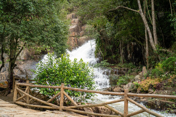 A serene waterfall surrounded by lush greenery and wooden fencing.