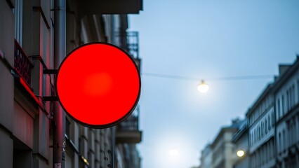 Bright red circular illuminated sign glowing against a twilight sky and urban cityscape background.